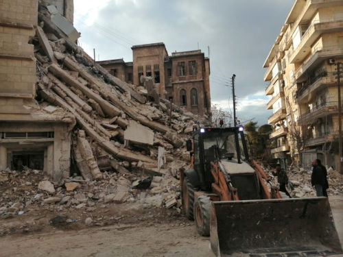 Blick auf die Trümmer eines eingestürzten Hauses. Ein Bagger steht davor